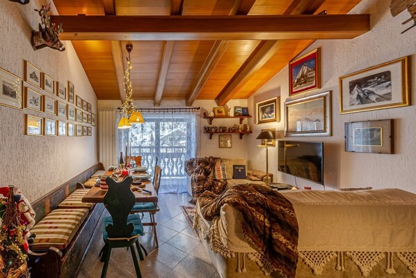 A cozy living room with a fireplace, a dining area with a long table, and a sofa with a blanket.