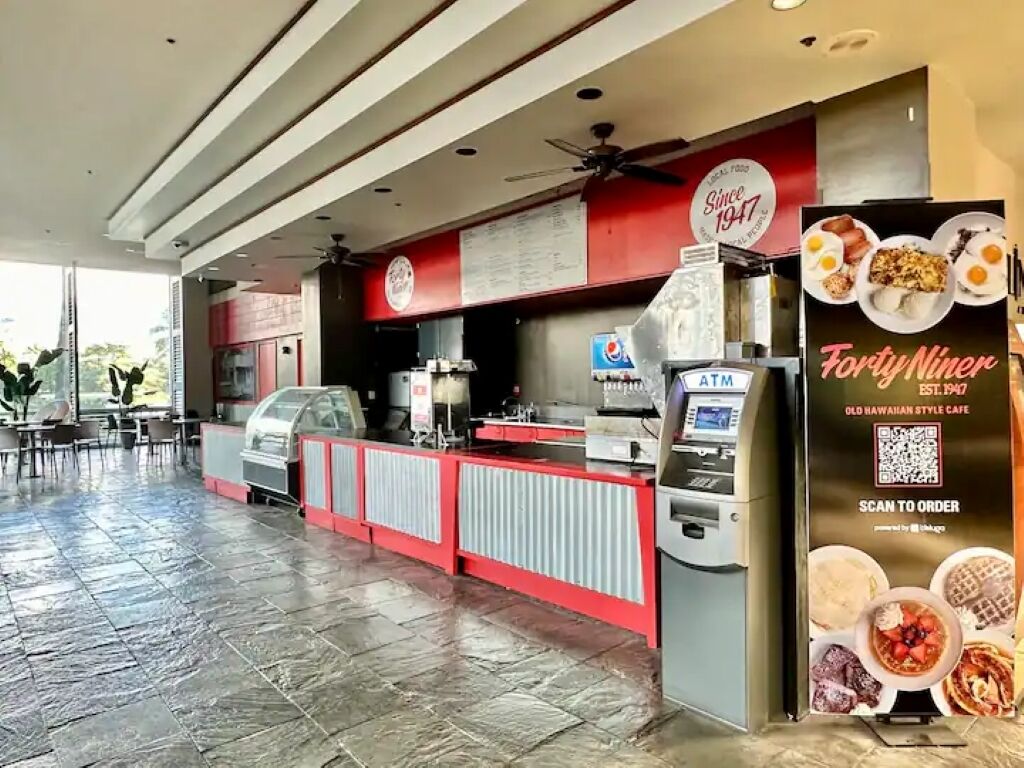 Una cafetería con decoración en rojo y blanco, un cajero automático y un cartel con la carta.
