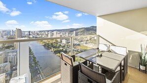 Ein Balkon mit Rattanmöbeln, einem Glastisch und Blick auf Stadt und Fluss.
