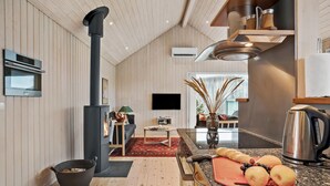 A modern kitchen with a wood stove, a flat-screen TV, and a dining area with a red rug. - Cozy home in Odder with WiFi (Odder)