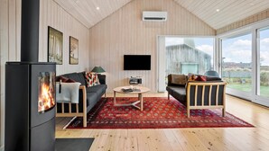 A cozy living room with a fireplace, a sofa, a coffee table, and a large window offering a view of the outdoors. - Cozy home in Odder with WiFi (Odder)