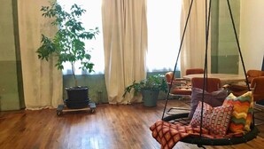A spacious room with a wooden floor, a hanging swing chair with patterned cushions, and two potted plants. - Downtown Lynchburg *REAL loft living* Va Virginia (Lynchburg)