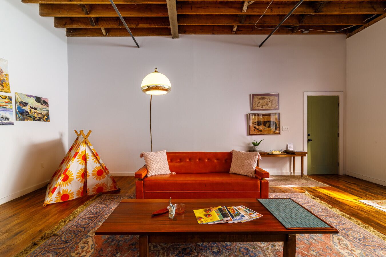 A cozy living room with a red sofa, a wooden coffee table, a hanging lamp, and a colorful rug.