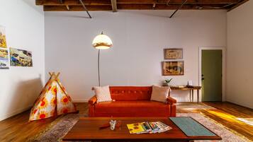 A cozy living room with a red sofa, a wooden coffee table, a hanging lamp, and a colorful rug.