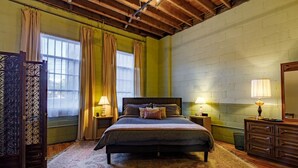 A bedroom with a bed, two bedside tables with lamps, a dresser, a window with curtains, and a patterned rug. - Downtown Lynchburg *REAL loft living* Va Virginia (Lynchburg)