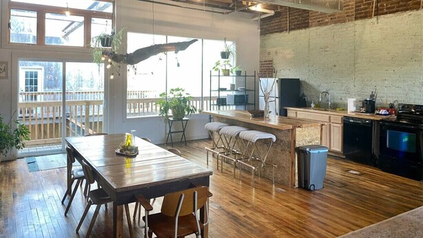 A spacious kitchen with wooden flooring, a dining area with a wooden table and chairs, and a brick wall. - Downtown Lynchburg *REAL loft living* Va Virginia (Lynchburg)