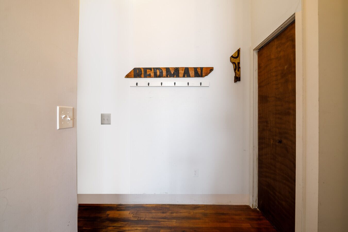 A hallway with a wooden floor, a white wall, and a door with a wooden frame.