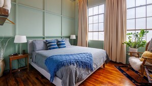 A bedroom with a bed, two bedside tables, a window with curtains, a plant, and a chair. - Downtown Lynchburg, Panel Loft, LYH Va Virginia (Lynchburg)