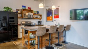 Une cuisine moderne dotée d’un coin bar, d’appareils électroménagers en acier inoxydable et de tabourets de bar en bois.