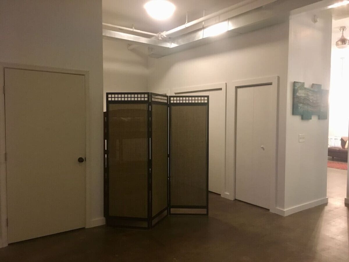 Un couloir avec deux portes blanches, une cloison vitrée et un plafond laissant apparaître les conduits.