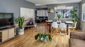 A modern living room with a flat-screen TV, wooden coffee table, and a dining area with a table and chairs. - Welcome to Ho'onani Pua Hale (Waipahu)