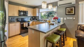 A modern kitchen with a central island, stainless steel appliances, and pendant lighting. - Welcome to Ho'onani Pua Hale (Waipahu)