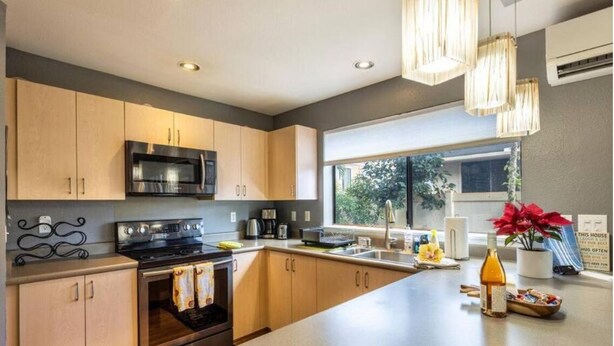 A modern kitchen with a large island, stainless steel appliances, and a view of greenery outside. - Welcome to Ho'onani Pua Hale (Waipahu)