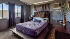 A bedroom with a bed, a nightstand, a dresser, a window with curtains, and a wall-mounted air conditioner. - Welcome to Ho'onani Pua Hale (Waipahu)