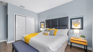 Una camera da letto con un letto, comodini, una panca, un armadio e opere d'arte alle pareti.