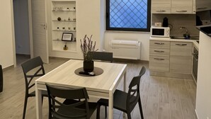 A modern kitchen with a dining area, featuring a white table with black chairs, a potted plant, and a large window with a view. - DOMVS Ginori,Testaccio (Roma)