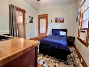 Un dormitorio con cama, escritorio de madera, ventana y puerta.