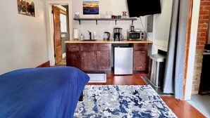 Habitación compacta con cama, kitchenette con microondas, cafetera y televisor fijado a la pared.