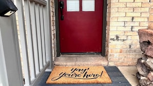 Una puerta roja con un felpudo que dice “¡yay! ¡estás aquí!”