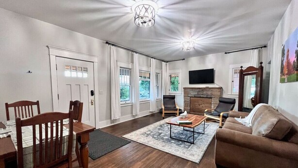 A spacious living room with hardwood flooring, a fireplace, a dining area with a table and chairs, and large windows with curtains. - Relaxing Historic Home in Downtown Pet Friendly (Flagstaff)