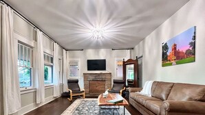 A living room with a fireplace, a brown leather sofa, two armchairs, a coffee table, and a large flat-screen TV mounted on the wall. - Relaxing Historic Home in Downtown Pet Friendly (Flagstaff)