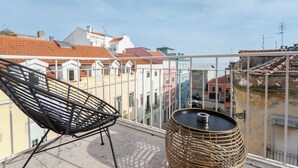 Un balcón con una silla de mimbre y una mesa redonda, con vistas a edificios coloridos.