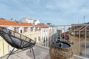 Varanda com cadeira de vime e mesa redonda, com vista para edifícios coloridos.
