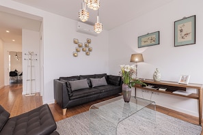 A modern living room with a black leather sofa, a glass coffee table, a wooden console table, and a wall-mounted air conditioning unit.