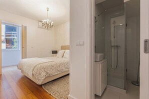 A bedroom with a bed, a chandelier, a nightstand, and a window with a view. - Cortes Apartment in Lisbon Historic (Lisbon)