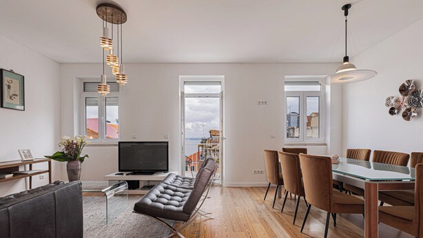 A modern living room with a sofa, TV, and dining area with chairs. - Cortes Apartment in Lisbon Historic (Lisbon)