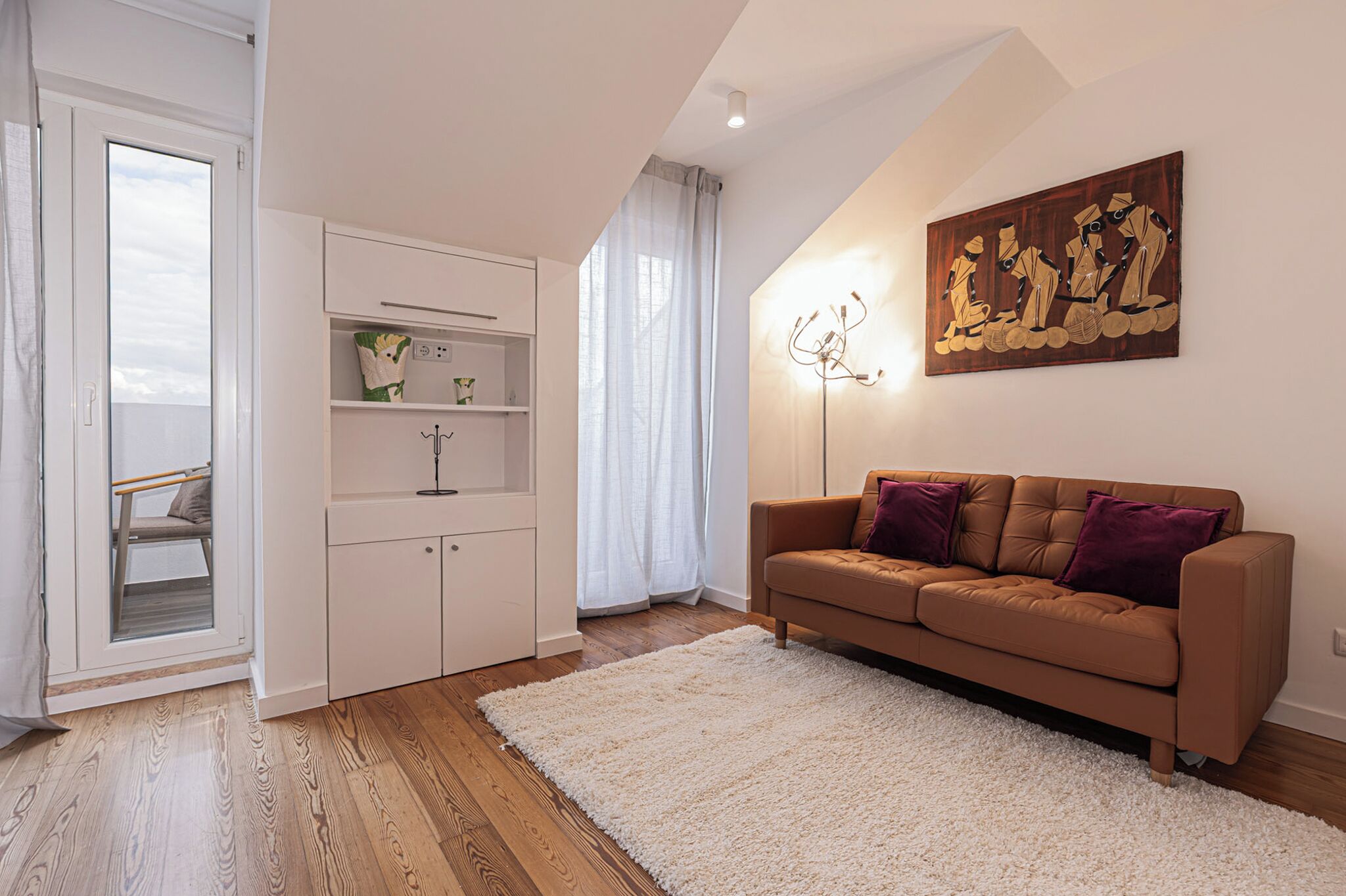 A modern living room with a sofa, a white rug, and a painting on the wall.