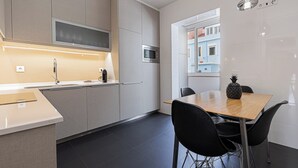 A modern kitchen with a built-in microwave, a wooden dining table with black chairs, and a view of a blue building through a window. - Cortes Apartment in Lisbon Historic (Lisbon)