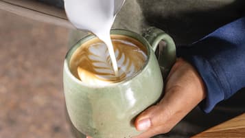Una mano che tiene una tazza di ceramica con decorazione a schiuma di latte.