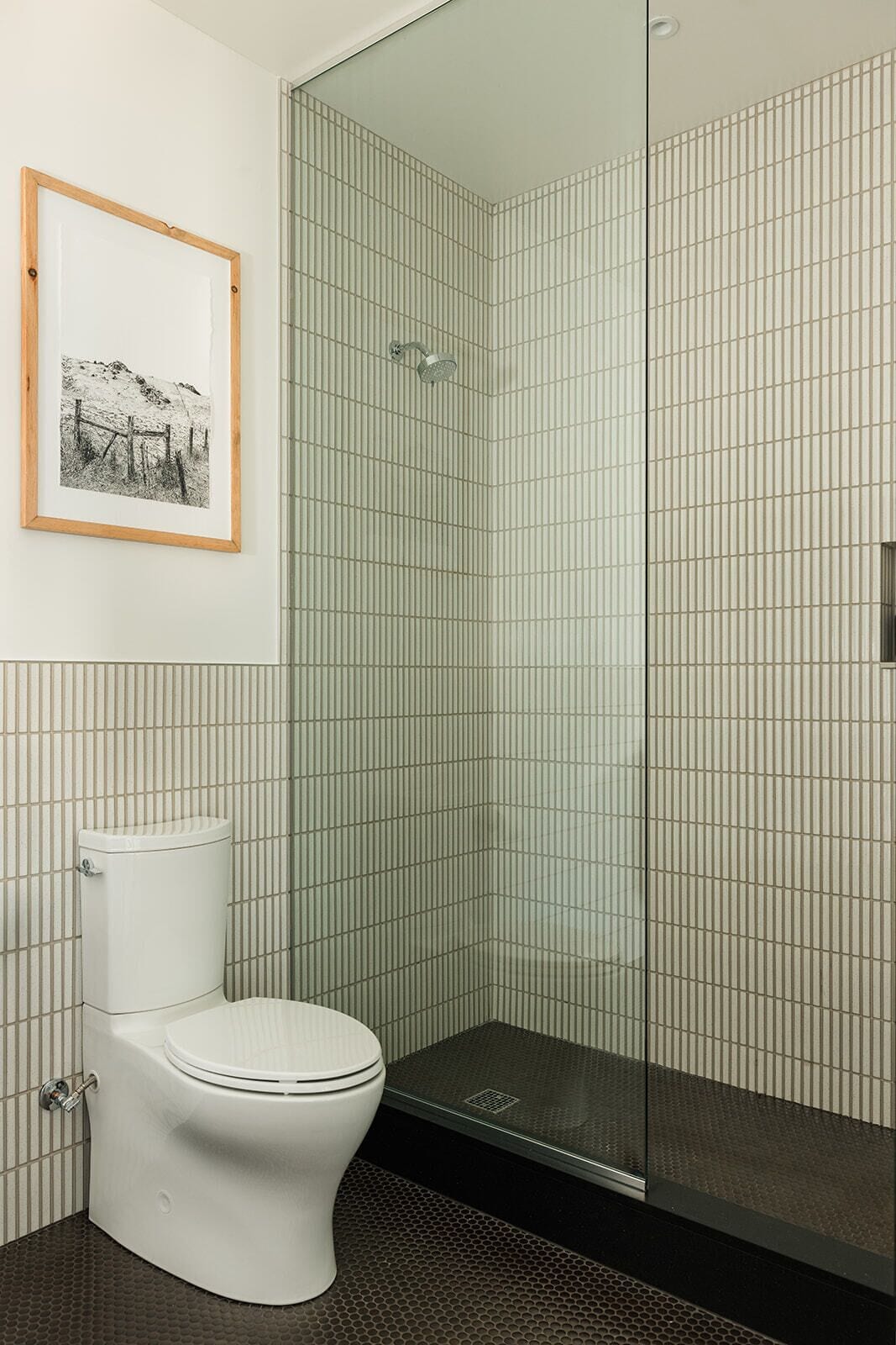 A modern bathroom with a toilet, a shower with a glass door, and a framed picture on the wall.