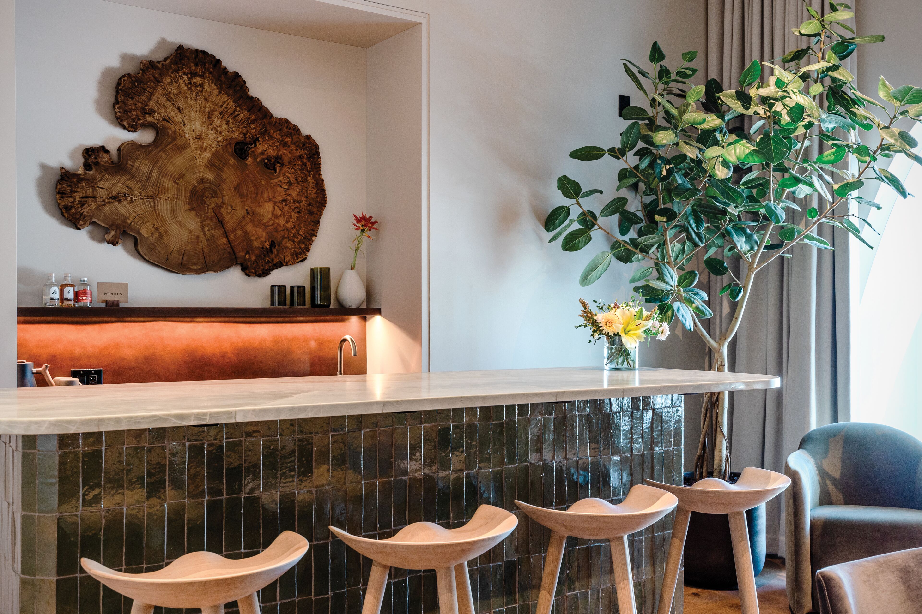 A modern kitchen with a large wooden wall art piece, a bar area with stools, and a potted plant.