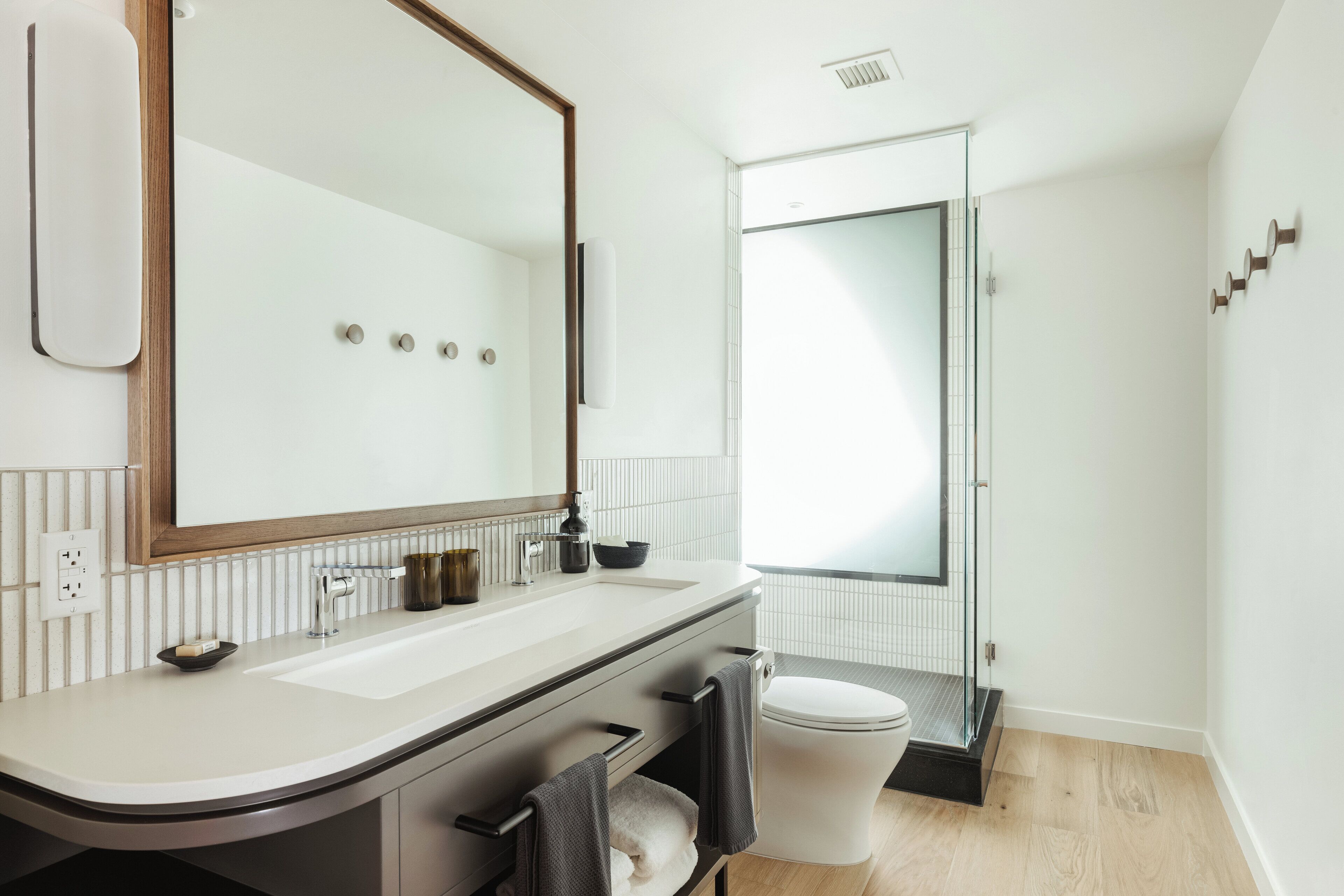 Un baño moderno con un espejo grande, lavamanos blanco y cabina de ducha de vidrio.