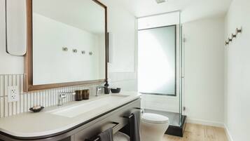 Un baño moderno con un espejo grande, lavamanos blanco y cabina de ducha de vidrio.
