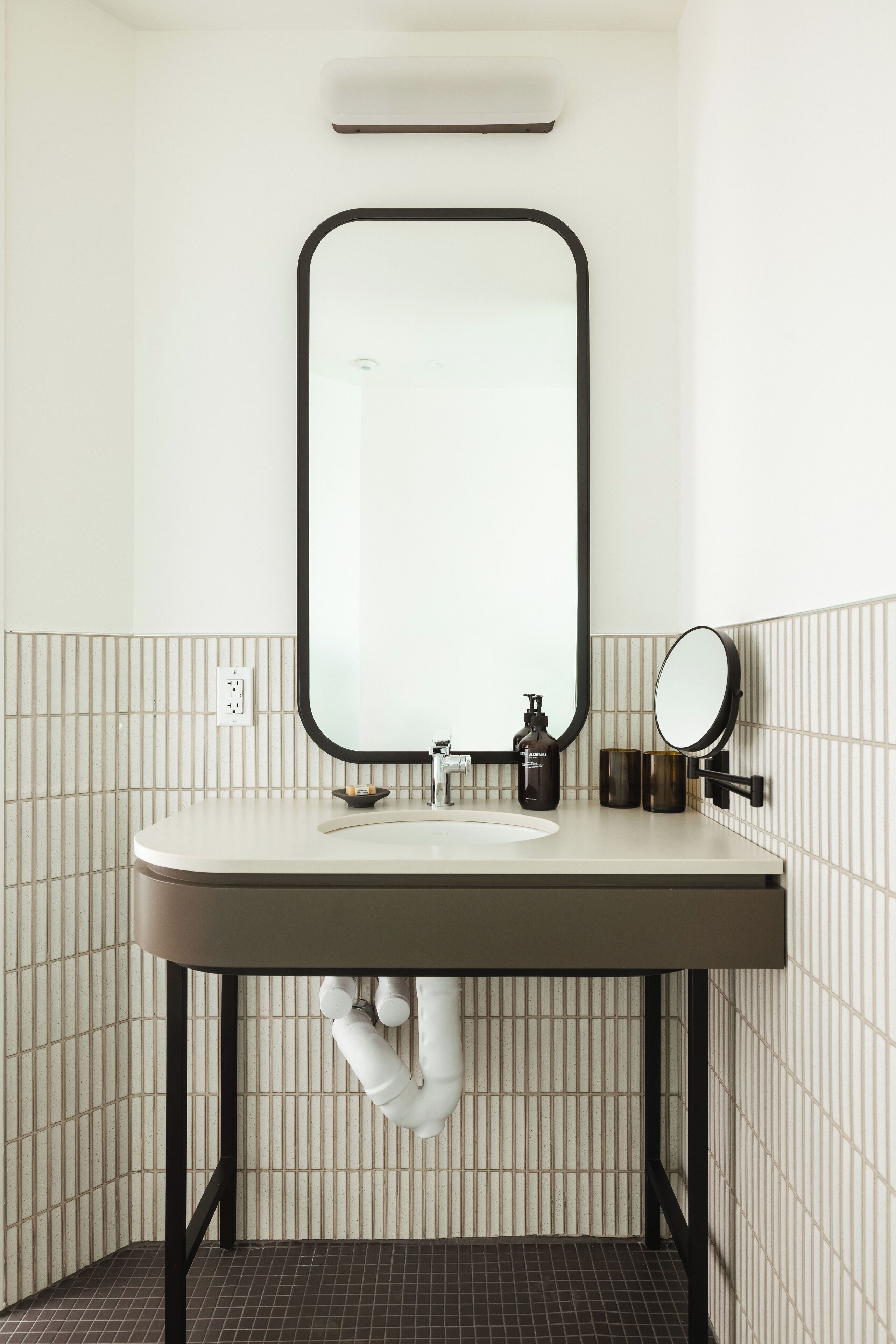 A bathroom with a white sink, black pipes, and a mirror.