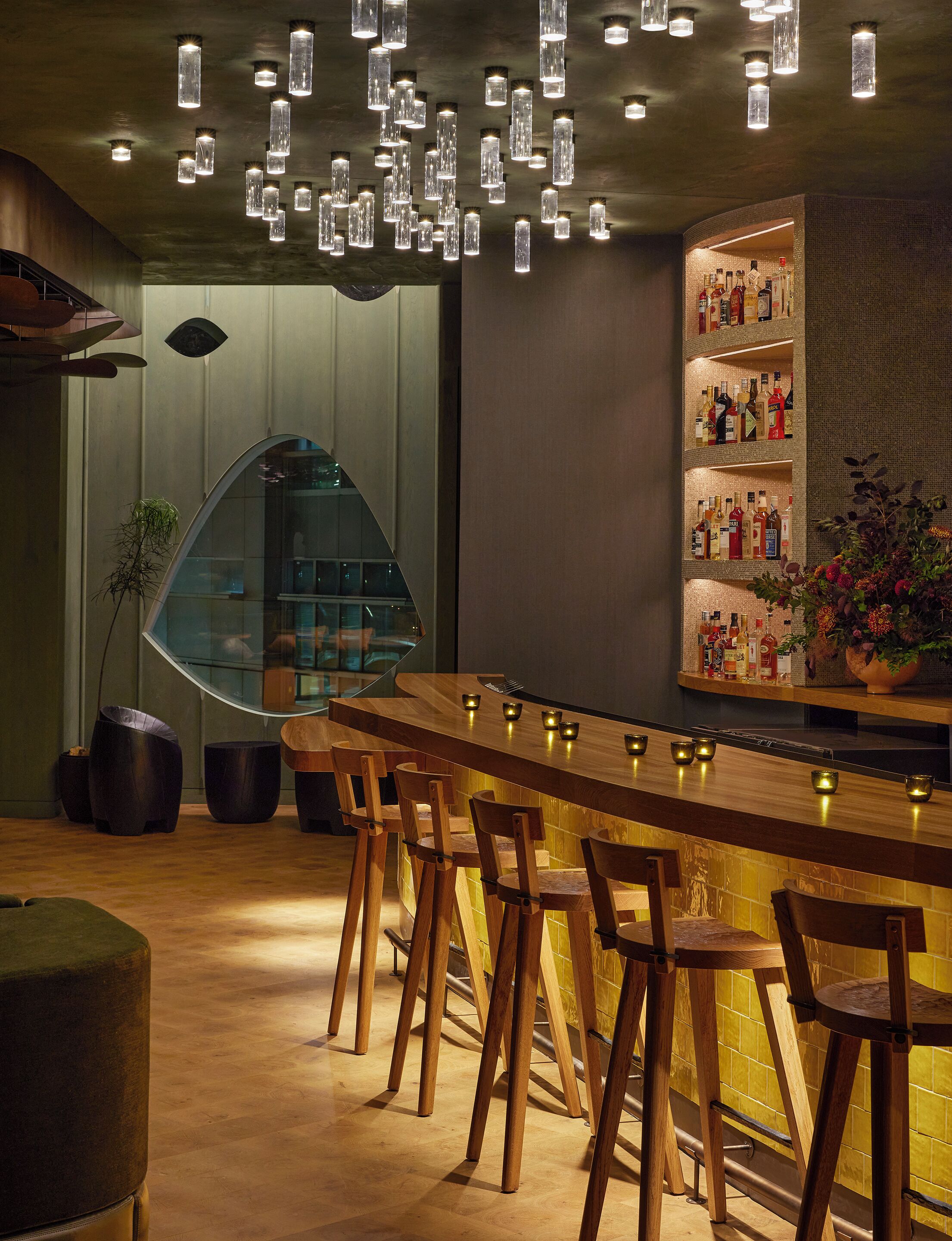 A bar area with wooden stools, a curved bar counter, and hanging pendant lights.