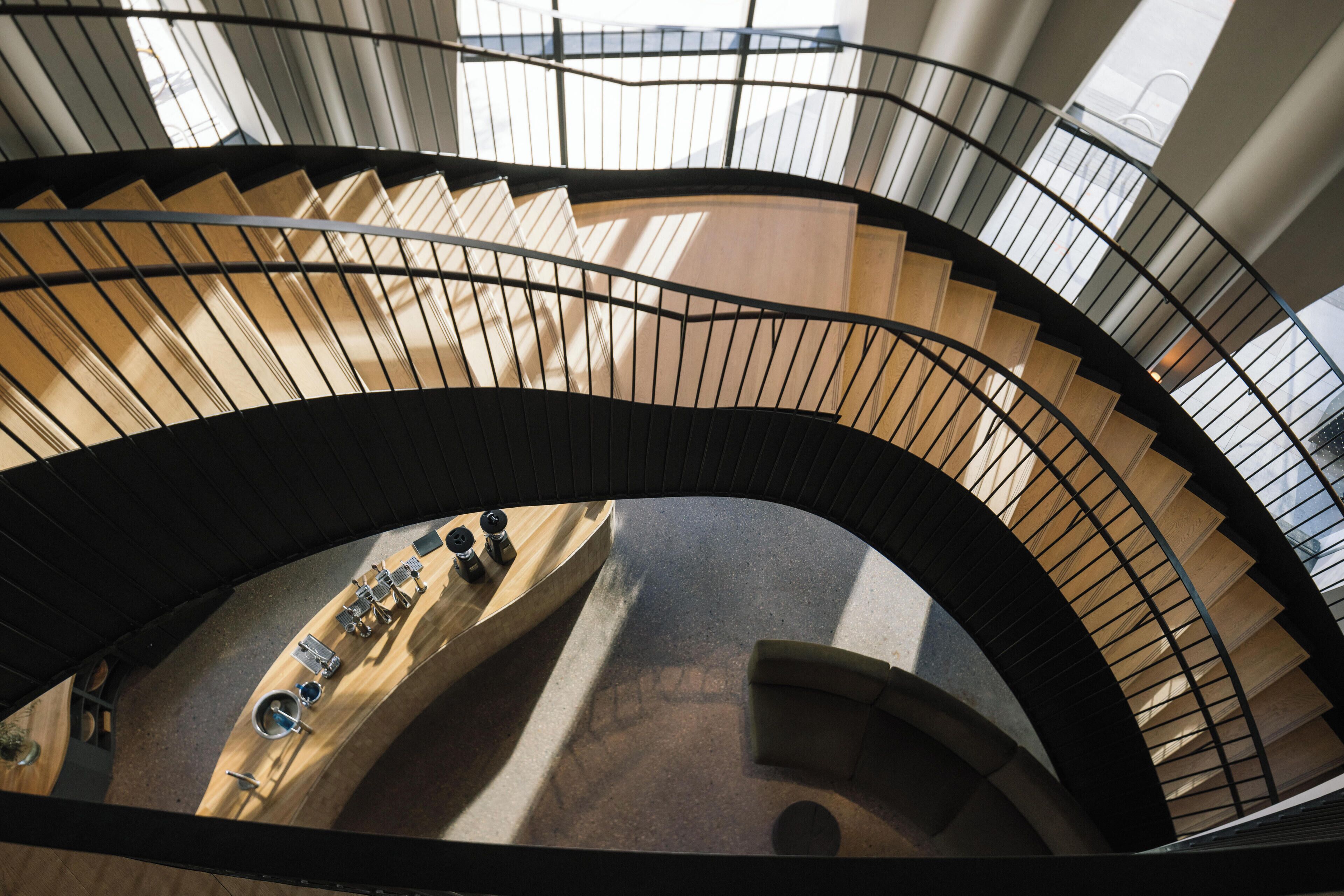 A spiral staircase with a curved railing and a view of a wooden floor and a seating area below.