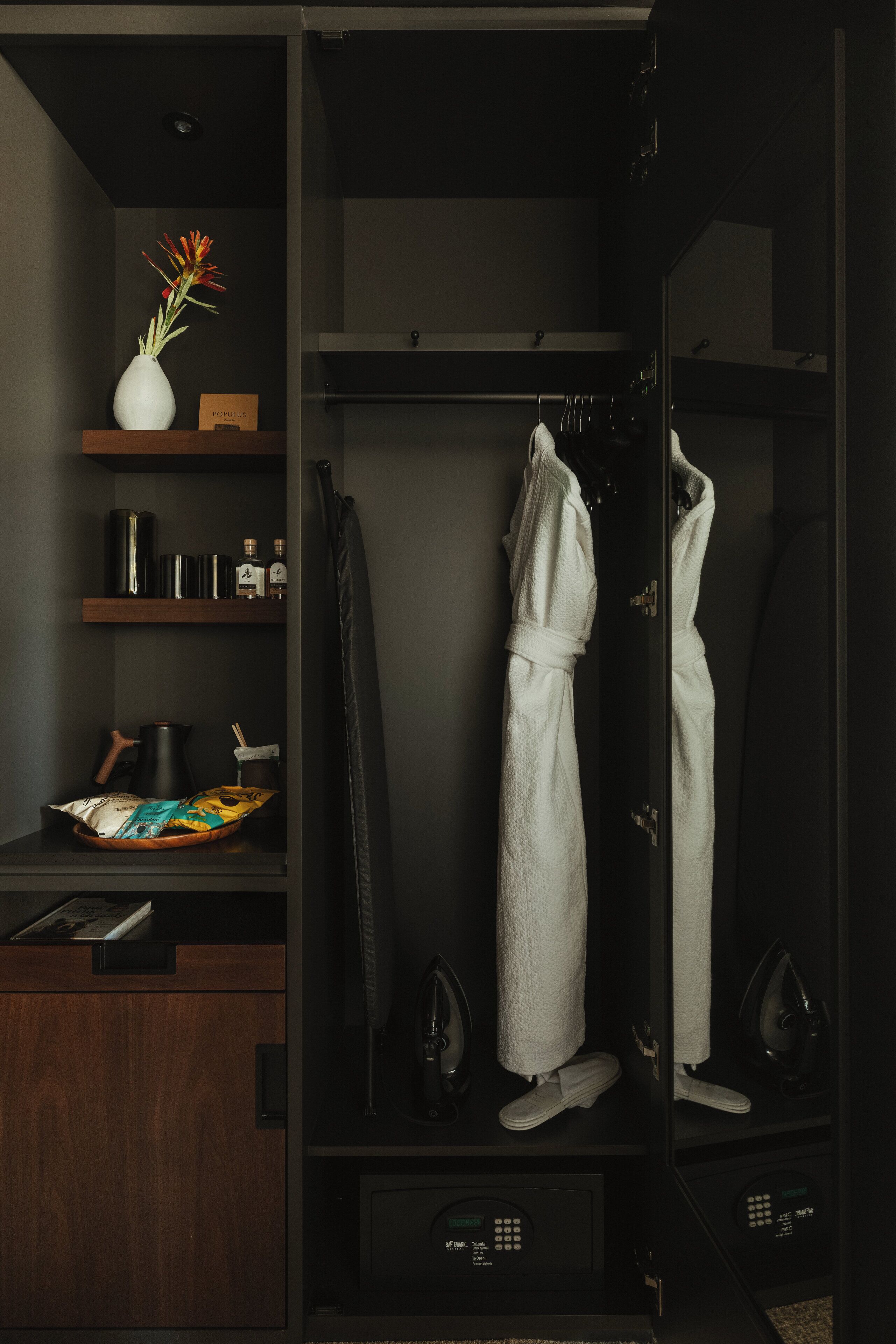 A walk-in closet with a robe hanging, a mirror, and shelves with books and a vase.