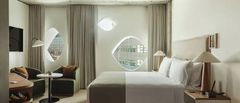 Une chambre d’hôtel moderne dotée d’un grand lit, de deux coins salon, d’une fenêtre ronde et d’un téléviseur.