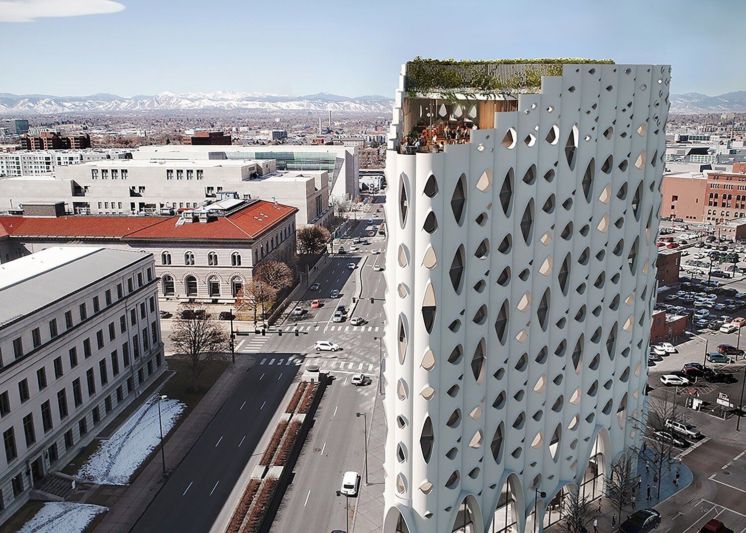 Un edificio moderno con una fachada perforada singular, un edificio de techo rojo al fondo, y una vista despejada del paisaje urbano circundante.