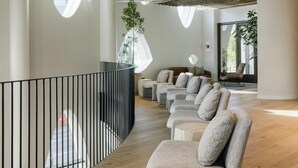 A modern interior with a wooden ceiling, a curved balcony, and a seating area with sofas and a chair.