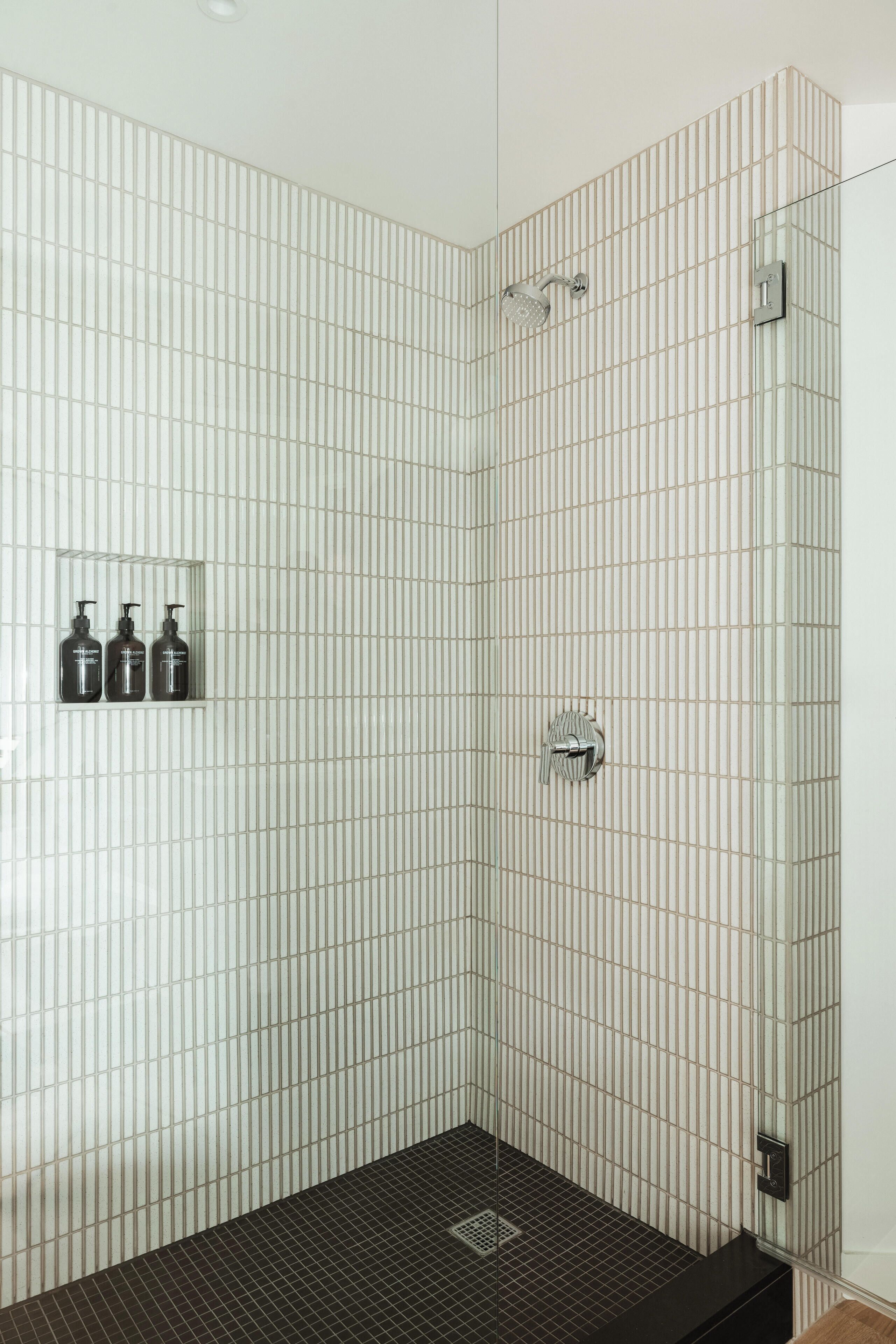 A shower with a tiled wall, a black floor, and a hand dryer.