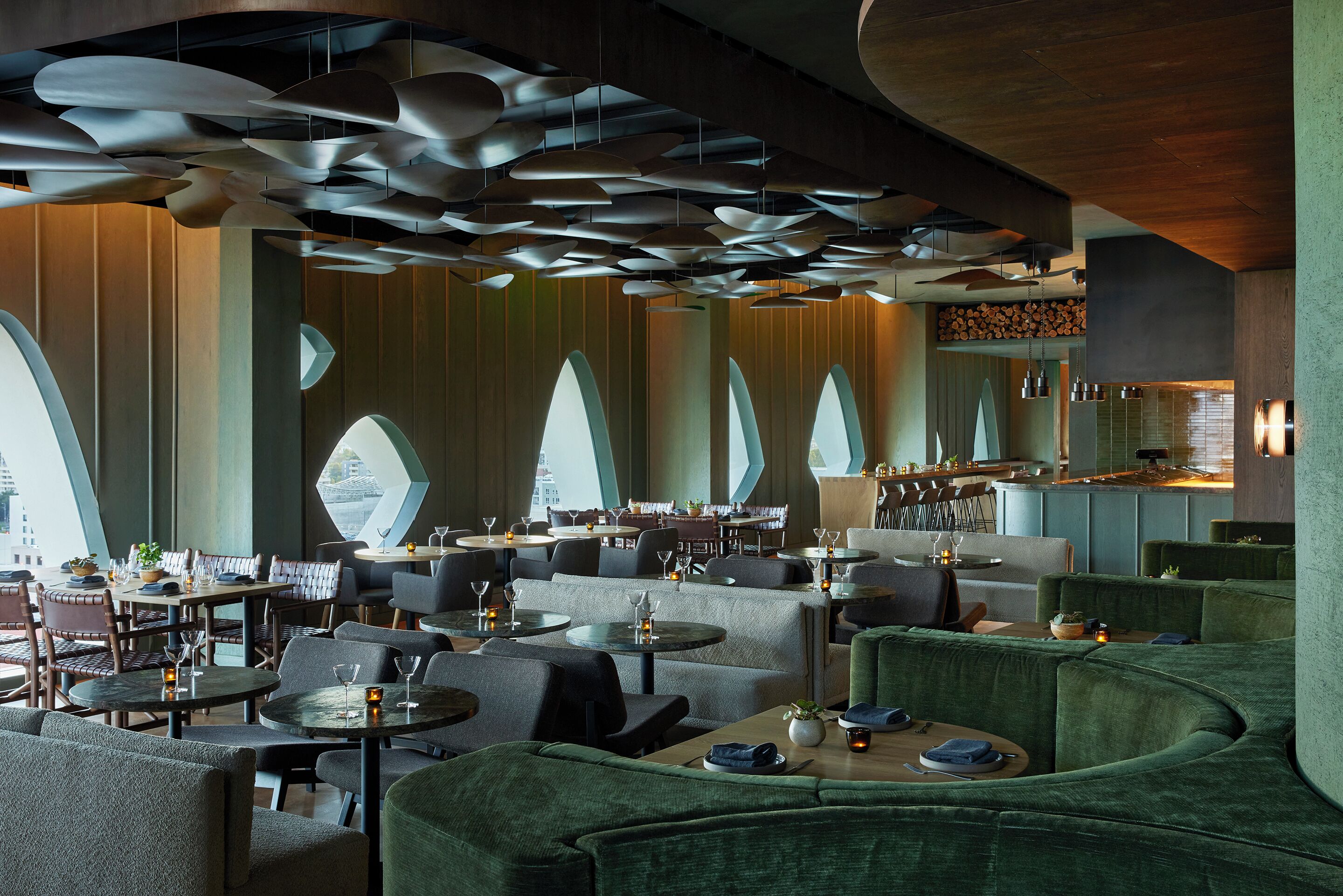 A modern restaurant with high ceilings, unique lighting fixtures, and a mix of seating arrangements including tables and couches.