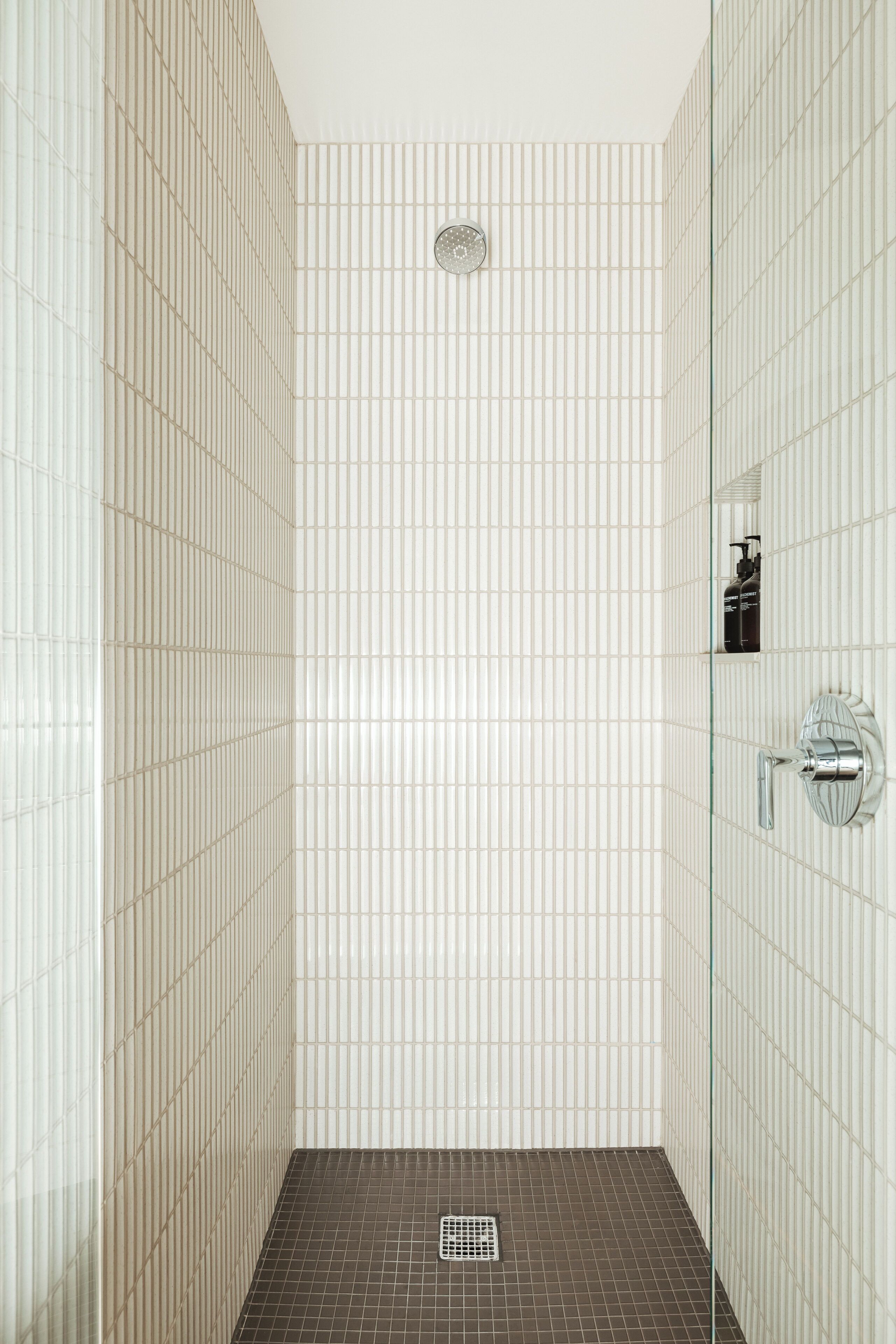 Un baño con piso de baldosas, zona de ducha y mampara de vidrio.