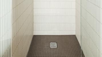 Un baño con piso de baldosas, zona de ducha y mampara de vidrio.