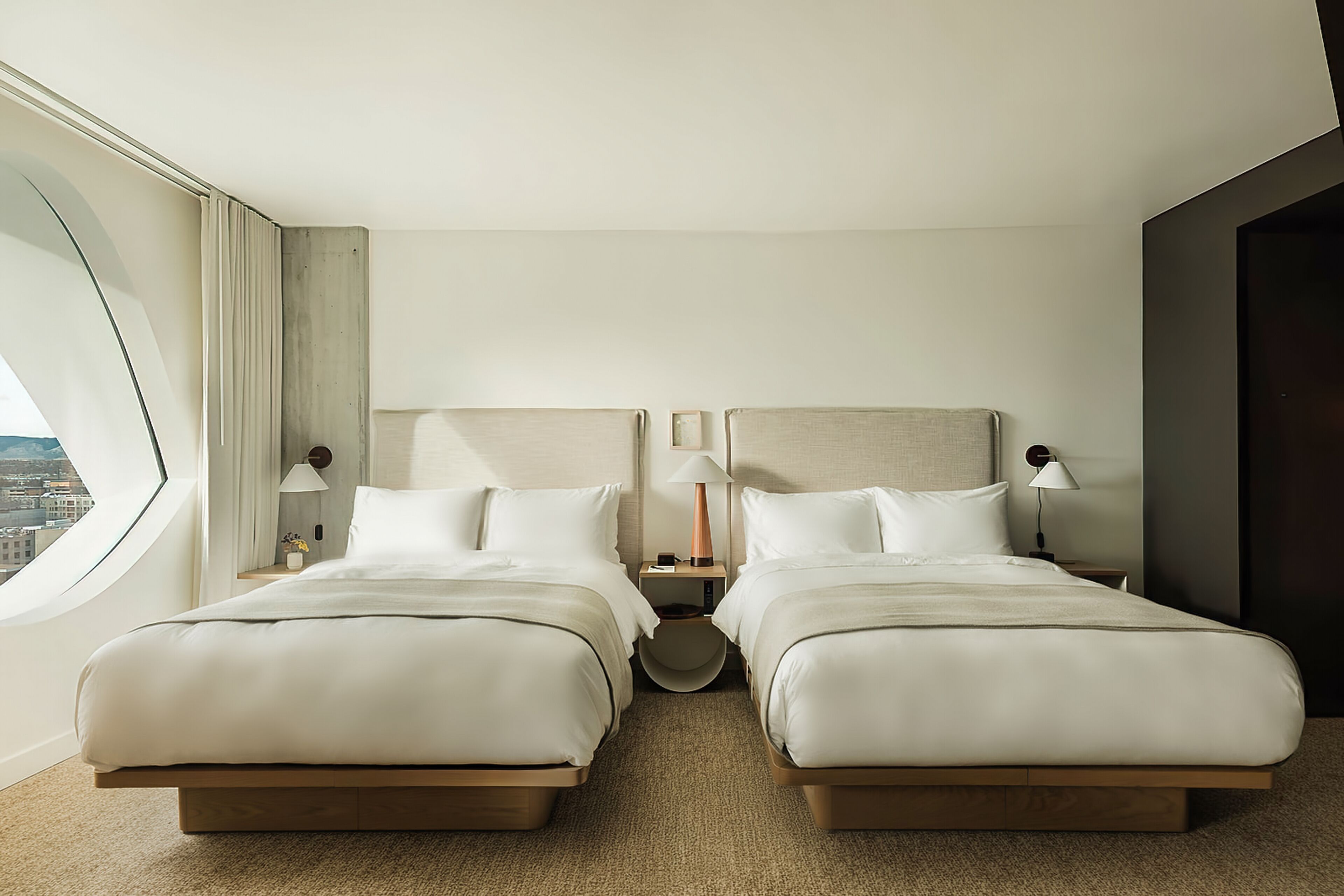 A hotel room with two beds, a round table, and a view of the city.