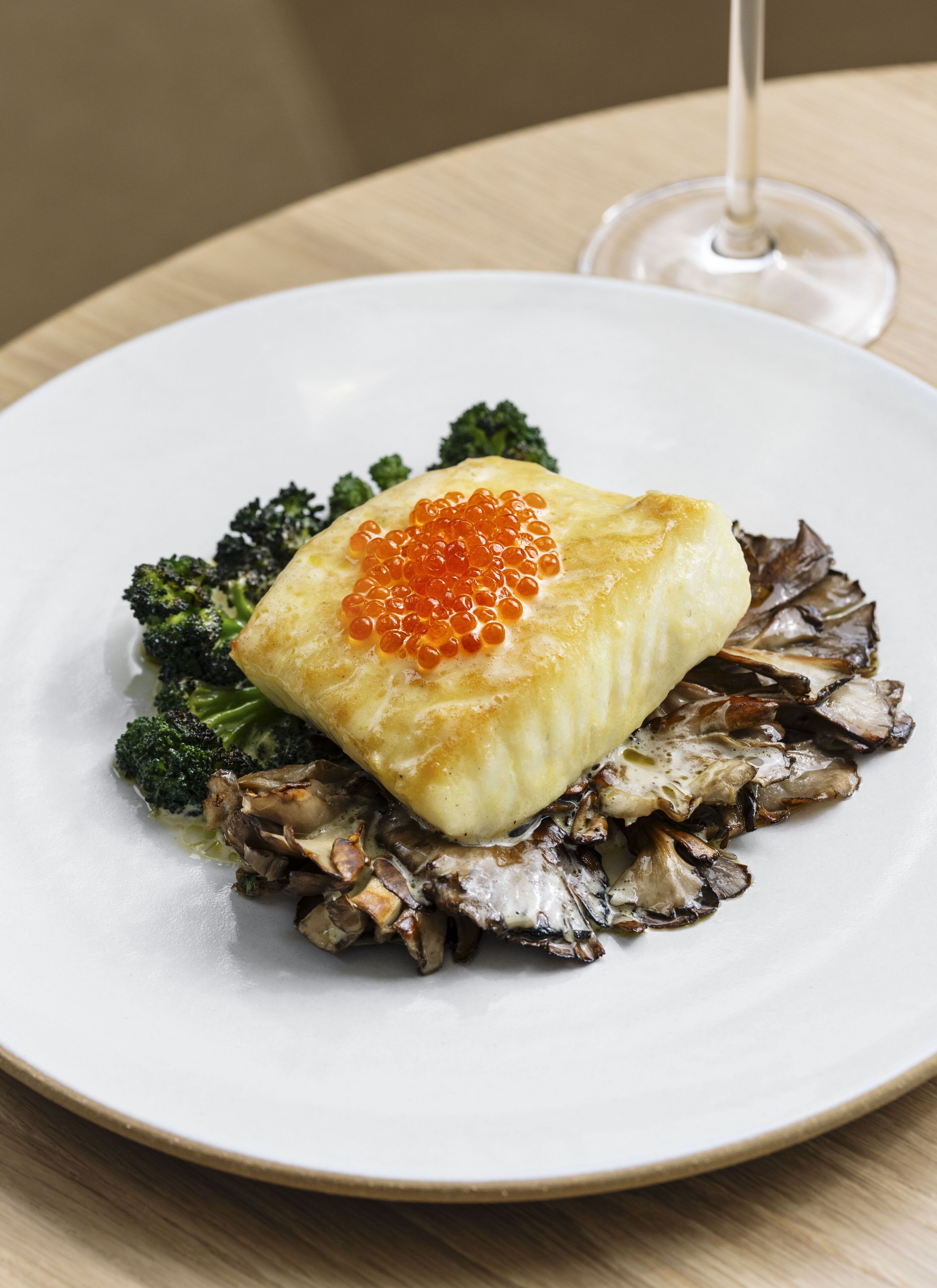 Une assiette contenant un morceau de poisson garni de caviar rouge, accompagné de brocolis et de champignons.